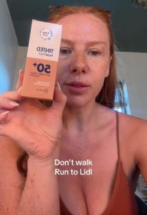 Woman holding up a bottle of Cien tinted facial fluid SPF 50+.