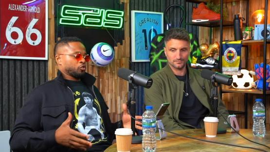 Two men sitting at a table, talking into microphones.