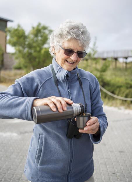 Smiling senior woman pouring coffee from a thermos.