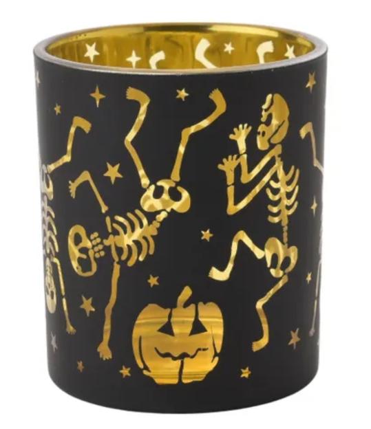 Black and gold Halloween candle holder with dancing skeletons and a jack-o'-lantern.