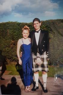 Photo of a couple at a prom; the woman is wearing a blue dress and the man is wearing a kilt.