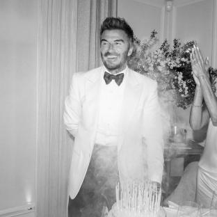 Black and white photo of David Beckham at his 50th birthday party, standing in front of a birthday cake.