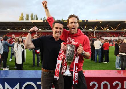 Rob McElhenney and Ryan Reynolds holding a trophy at a soccer game.