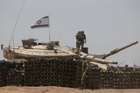 Israeli soldiers standing on a tank with ammunition in the foreground.