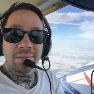 Selfie of a man wearing sunglasses and a headset in a small plane above the clouds.