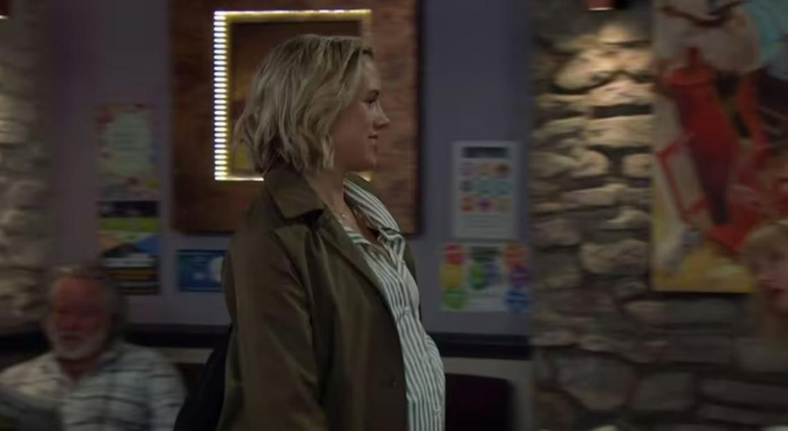 A pregnant woman in a green coat and striped shirt.