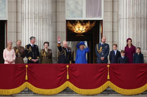 King Charles, Queen Camilla, and their family waving from Buckingham Palace balcony.