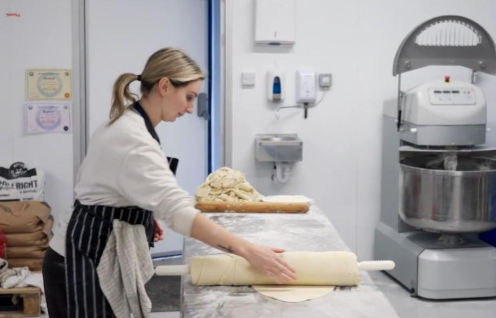 Woman rolling out dough in a bakery.