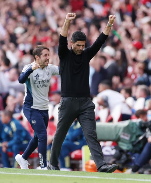 Arsenal manager Mikel Arteta celebrates a goal with his arms raised, while another staff member cheers behind him.