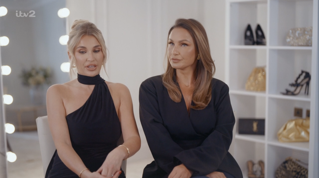 Screenshot of two women in black outfits sitting and talking.
