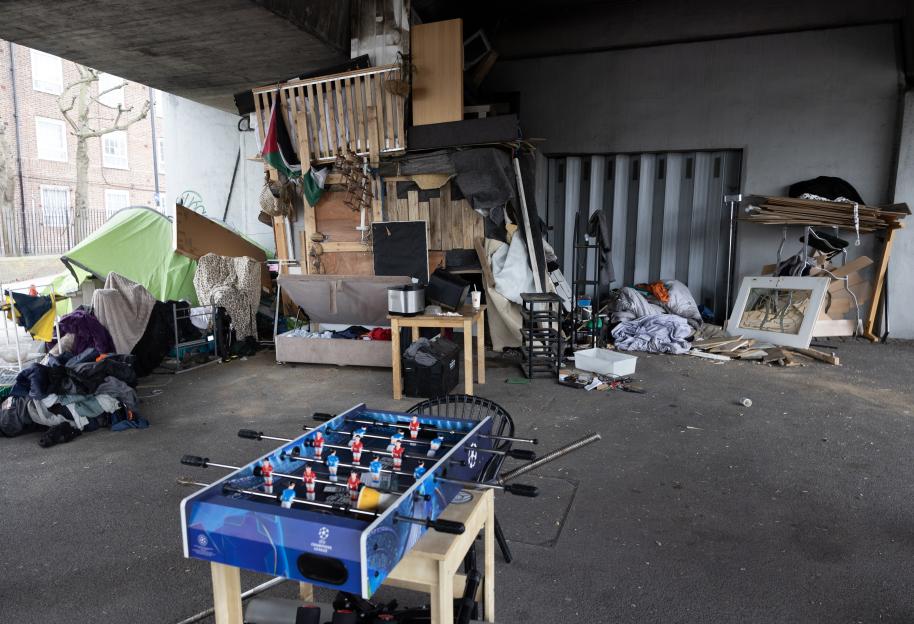 Foosball table in front of makeshift homeless encampment under bridge.