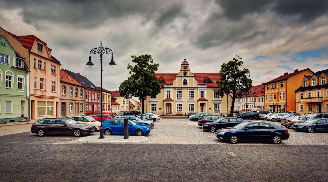 Town square in Eisenhuettenstadt, Germany, with cars parked and colorful buildings.