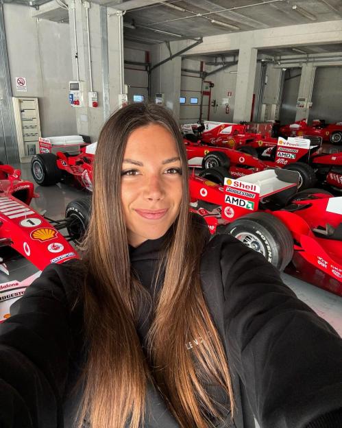 Laura Villars in a garage filled with Ferrari Formula 1 race cars.