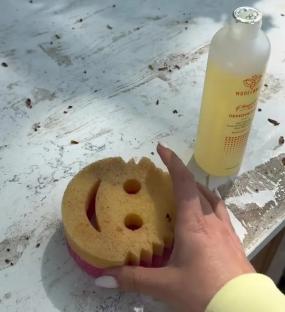 Cleaning a dirty countertop with a smiley-face sponge and cleaning solution.