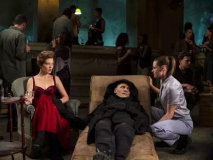 Scene from Crimes of the Future showing a man lying on a chaise lounge while two women attend to him.