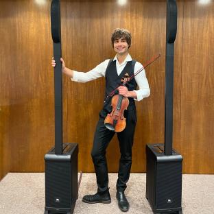 Alexander Rybak holding a violin between two speakers.