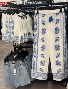White pants and top with blue embroidery displayed on a clothing rack.