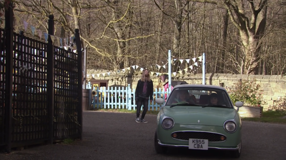 A light green car arriving at a gate with bunting.