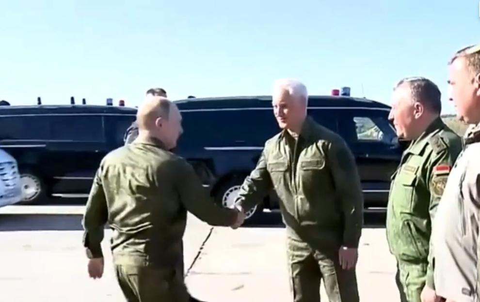 Putin shaking hands with another military official in front of a dark armored vehicle.