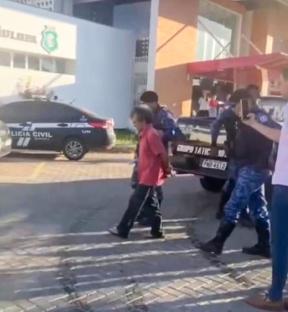 A man in handcuffs being escorted by police.