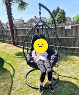 Person relaxing in a black egg chair in a garden.