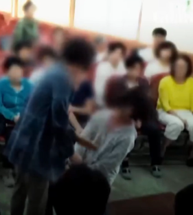 Blurry photo of a person being restrained by another person in a crowded room.