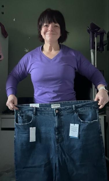 Woman holding up a pair of very large jeans after losing 16 stone.