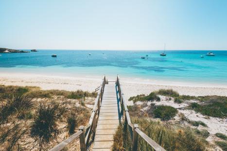 Wooden boardwalk leading to a sandy beach with turquoise water and boats.