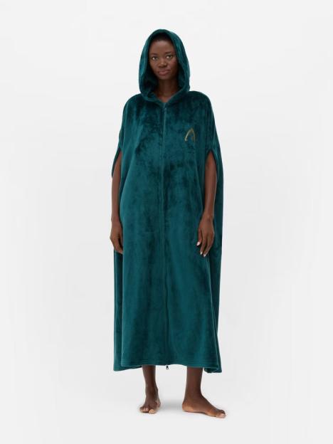 A Black woman wearing a teal hooded zippered cape with a golden logo.