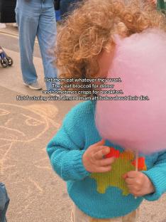 Child with curly hair eating cotton candy.