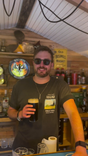 Iain Stirling holding a pint of dark beer in his home bar.