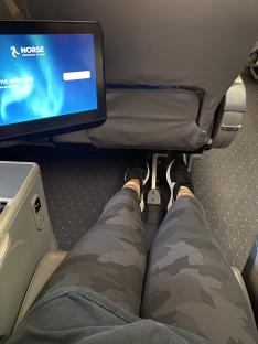 Person's legs in camouflage leggings on a Norse Premium Class airplane seat.