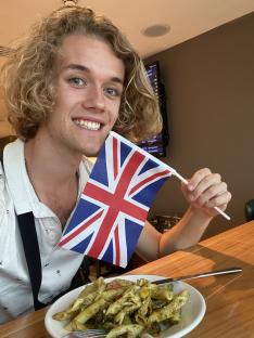 Person holding a UK flag and eating pesto pasta.
