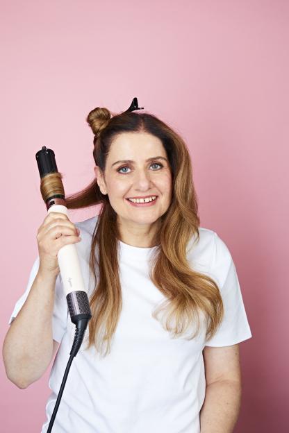 Woman using a Dyson Air Wrap to style her curly hair.