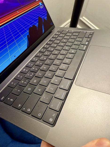 Close-up of a MacBook Pro M5 keyboard and trackpad, with a neon blue grid and cityscape on the screen.