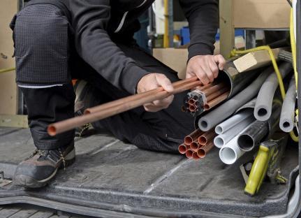 Construction worker sorting copper and other pipes in a vehicle.