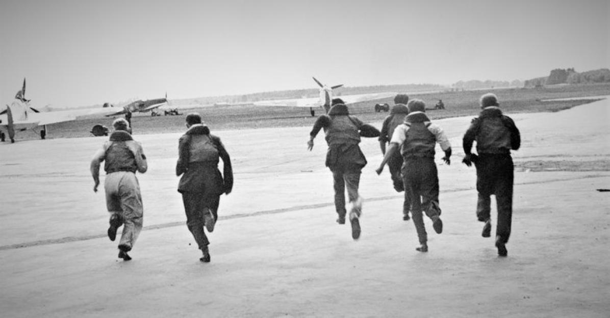Men running on an airfield toward airplanes.