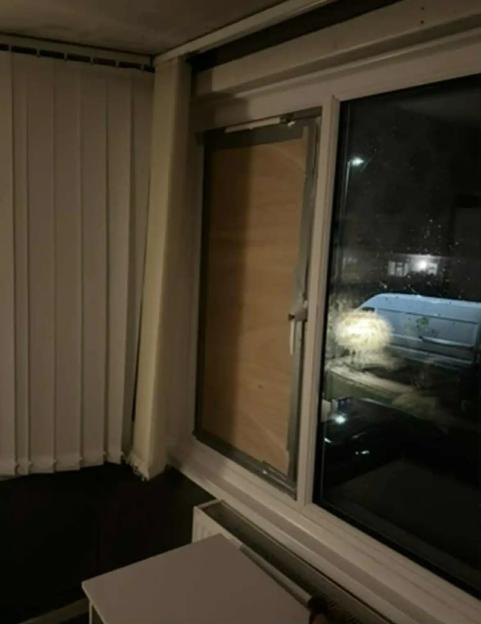 A window from inside a room with one pane boarded up and the other showing a dark exterior.
