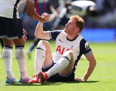 Dejan Kulusevski of Tottenham Hotspur sits on the field, assisted by a teammate.