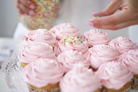 Pink cupcakes being decorated with sprinkles.