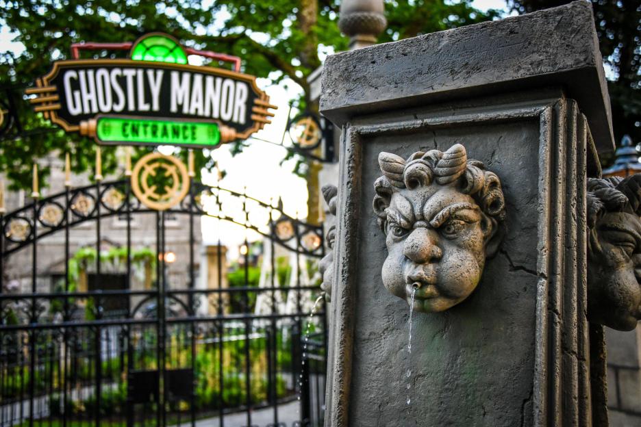 Ghostly Manor entrance sign at Paultons Park, with water spouting from a grotesque face carved into a stone pillar.