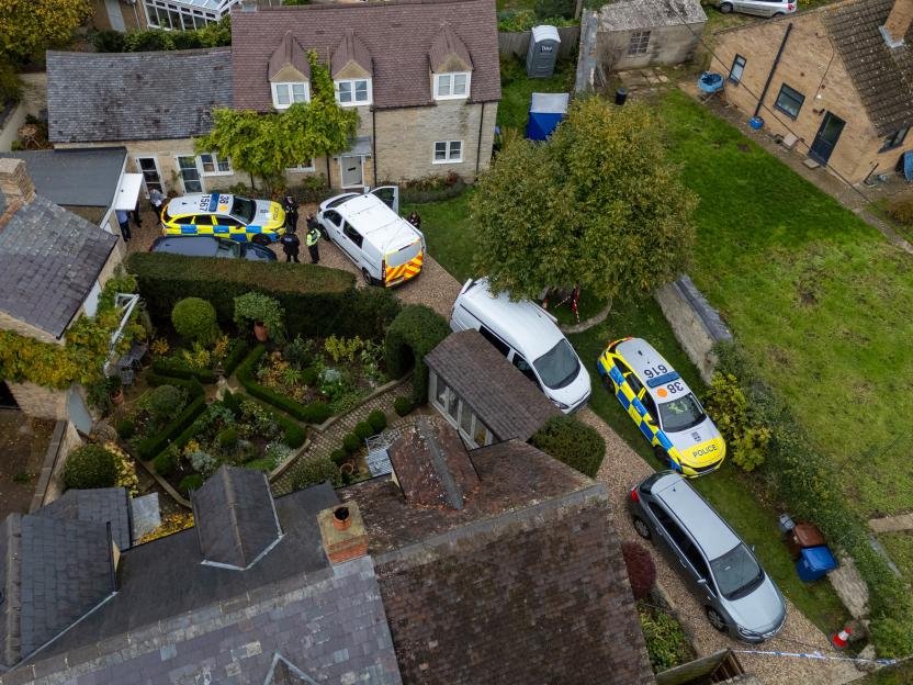 Aerial view of police cars and personnel at a property in Islip, UK, with a blue tent in the garden.