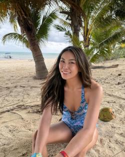 Woman sitting on a beach under palm trees wearing a swimsuit.