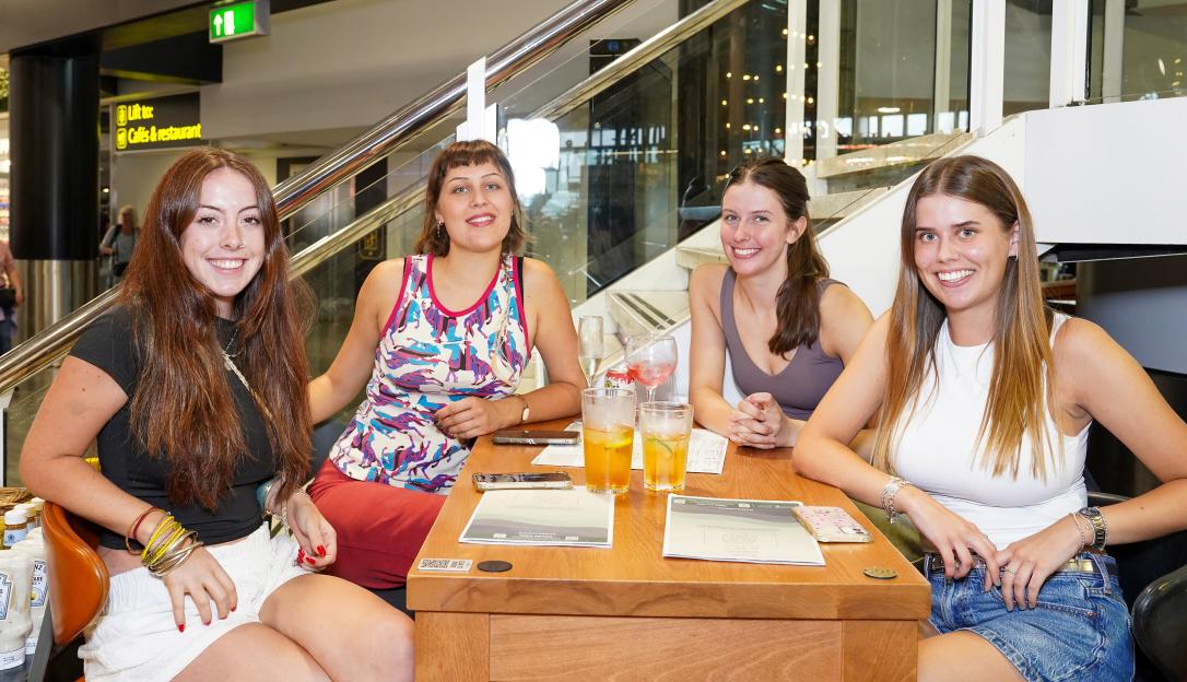 Four young women sitting at a table in a pub, enjoying drinks.