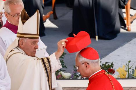 Pope Francis placing a red biretta on a new cardinal's head.