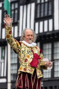 A man dressed as William Shakespeare waves.