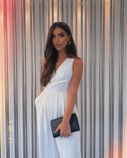 Woman in white jumpsuit holding a black clutch.