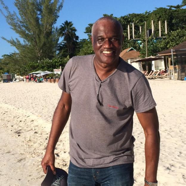 Charlene White's father Denniston smiling on a sandy beach.