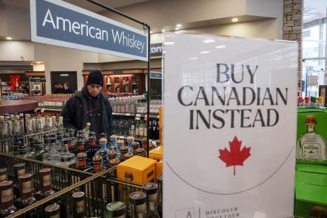 A customer holds a bottle of liquor in a store with a sign that says