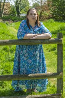 Woman in floral dress leaning on a wooden fence.